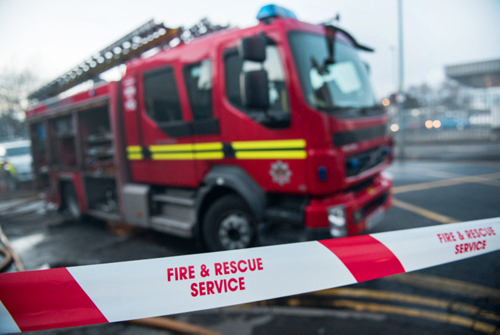 Red and white tape with the words Fire and Rescue Service with a Fire appliance in the background